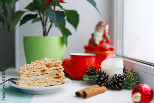 A piece of Christmas cake, a red mug of flower on the windowsill. Candle and cinnamon