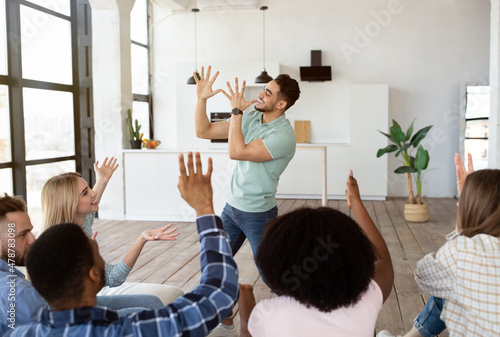 Young diverse friends playing charades game at home. Arab guy showing pantomime riddles, his fellow students guessing photo