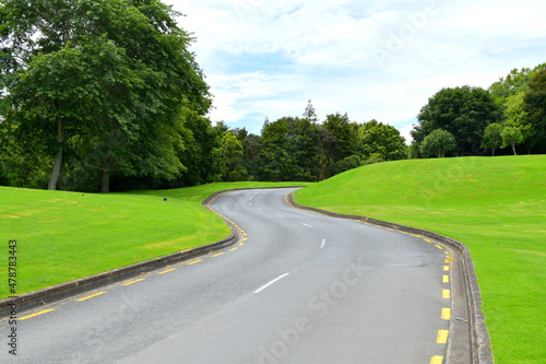 Asphalt road surrounded by bright green hills and trees during daylight