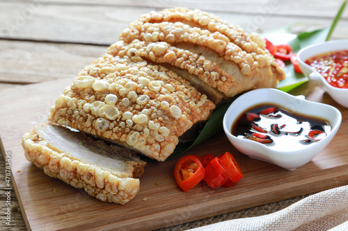 Closeup crispy pork belly or deep fried pork on wooden board with black soy sauce with red chili and spicy seafood sauce in background.