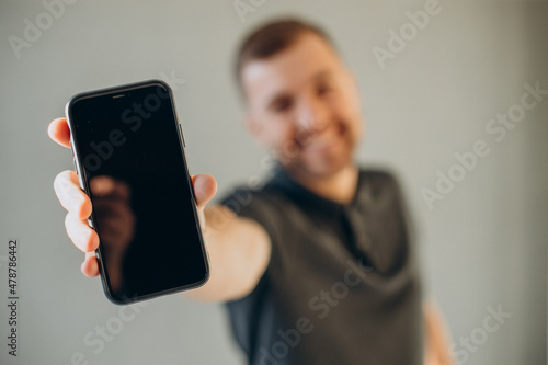 Handsome man holding mobile phone and showing it into camera