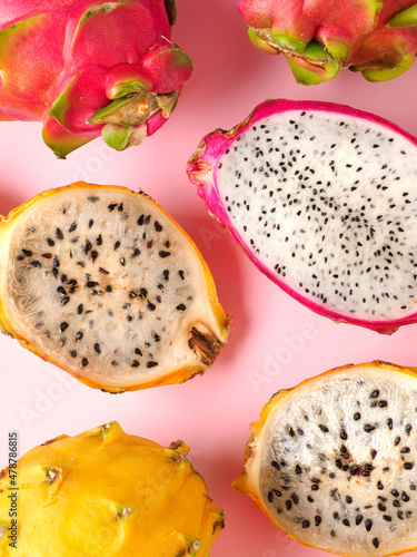 Delicious cut and whole dragon fruits pitahaya on color pink background. Sunny tropical photo with with exotic fruits and flowers. Composition with pitochaia. Space for text. Copy space. Top view
