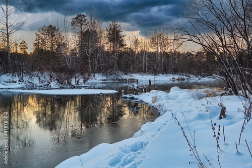 Winter landscape forest river with a bridge in the background at sunset.