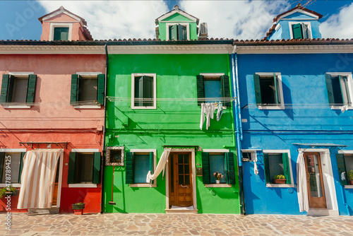 Red, green, blue houses of Burano island with small streets on sunny day. Venice area.