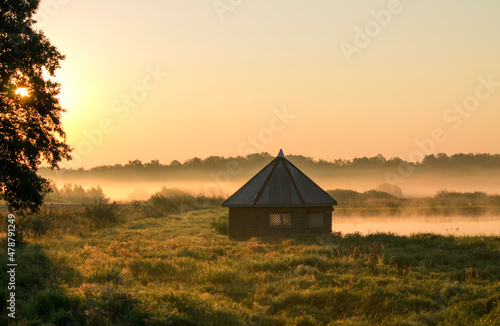A view on rural bower in the middle of wetlands during foggy morning sunrise. Warm colors.