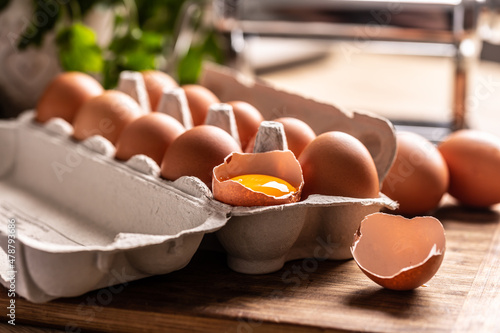 Fotografia A cardboard box full of fresh chicken eggs with yolk in broken egg on the kitche