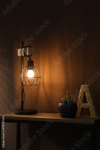 Stylish lamp, decor and green plant on wooden table near brown wall indoors. Interior design © New Africa