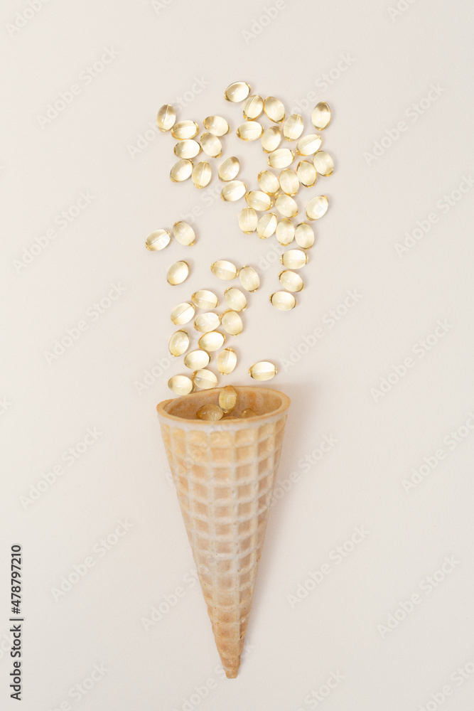 Ice cream cone and vitamins omega 3, D3 and fish oil capsules. Waffle cone. Vertical. Health care and medicine. Flat lay.