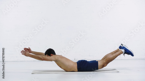 Slika na platnu full length of shirtless sportsman doing downward abs near white brick wall