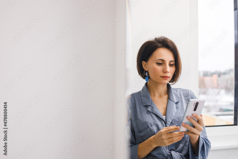 Bruinette woman in pajama working online with smartphone in hands at home. Female using phone looking at screen typing message, using telephone technology doing online job, surfing internet social Bruinette woman in pajama working online with smartphone in hands at home. Female using phone looking at screen typing message, using telephone technology doing online job, surfing internet social