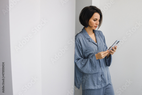 Photography Bruinette woman in pajama working online with smartphone in hands at home