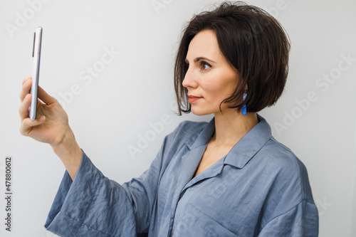 Bruinette woman in pajama working online with smartphone in hands at home. Female using phone looking at screen typing message, using telephone technology doing online job, surfing internet social photo