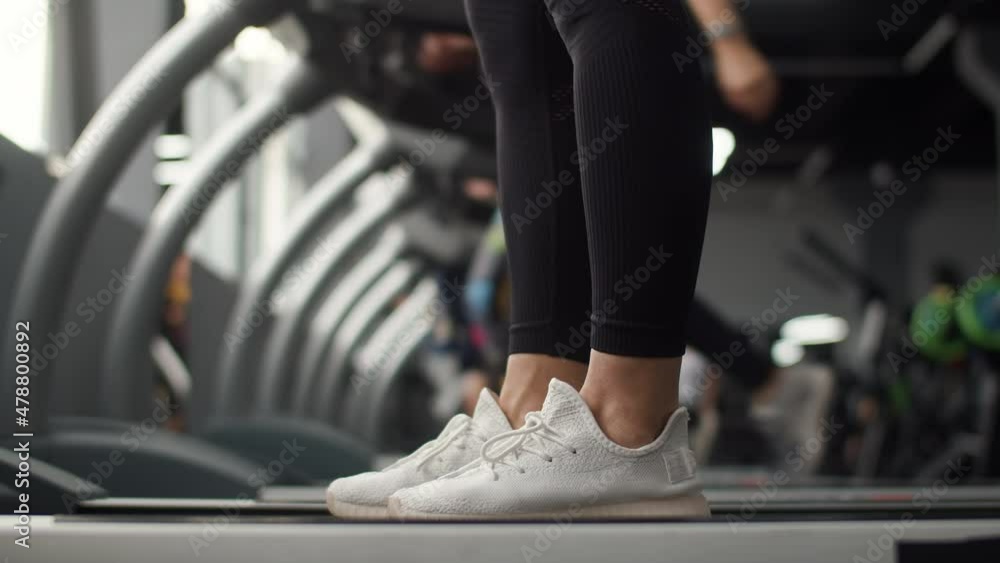 Closeup of legs woman jogging on treadmill in gym, side view. Woman trains in gym doing cardio workout on treadmill. Jogging concept Closeup of legs woman jogging on treadmill in gym, side view. Woman trains in gym doing cardio workout on treadmill. Jogging concept