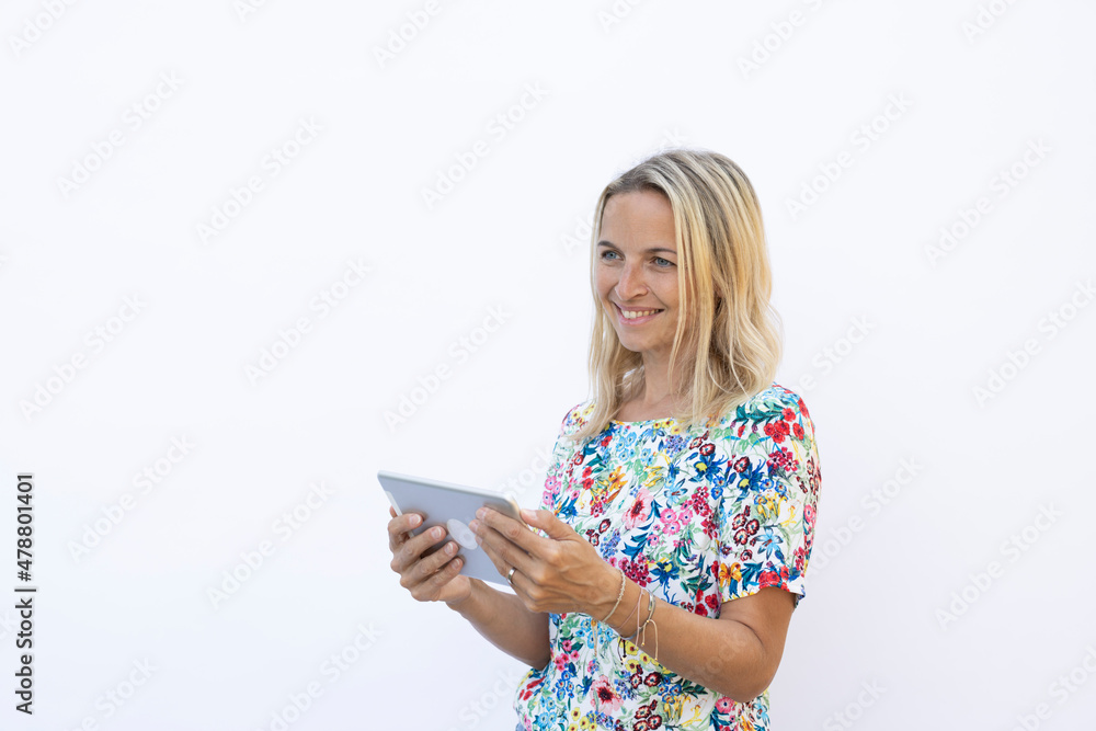 pretty young blonde woman with floral shirt is working with tablet in front of white background