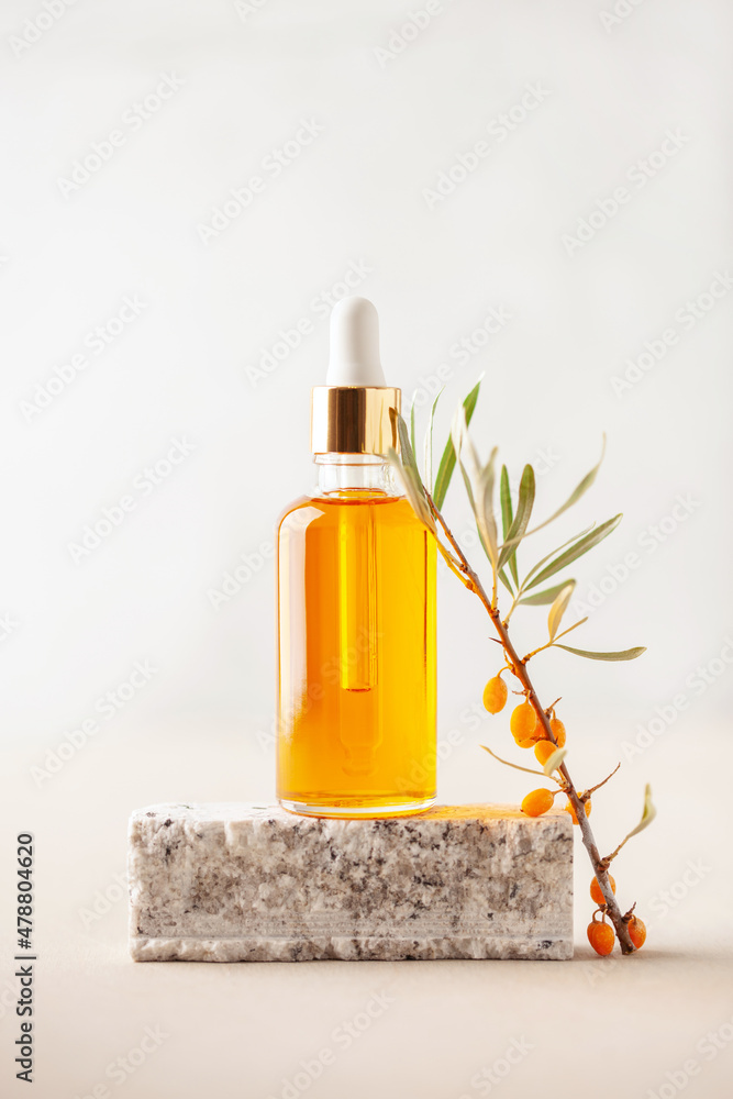 Essential oil and  branch of sea-buckthorn with berries and leaves on stone podium. Natural cosmetic