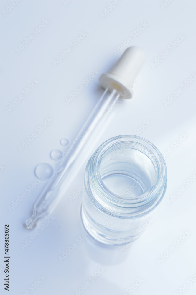 glass transparent jar and a cosmetic pipette with liquid droplets on a white background. glass transparent jar and a cosmetic pipette with liquid droplets on a white background.