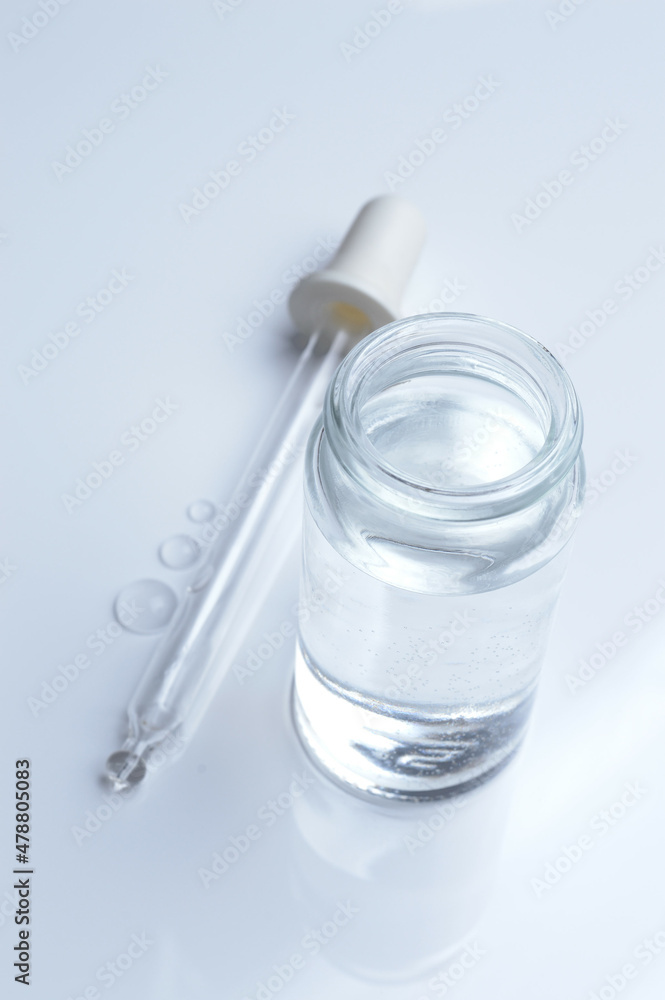 glass transparent jar and a cosmetic pipette with liquid droplets on a white background. glass transparent jar and a cosmetic pipette with liquid droplets on a white background.