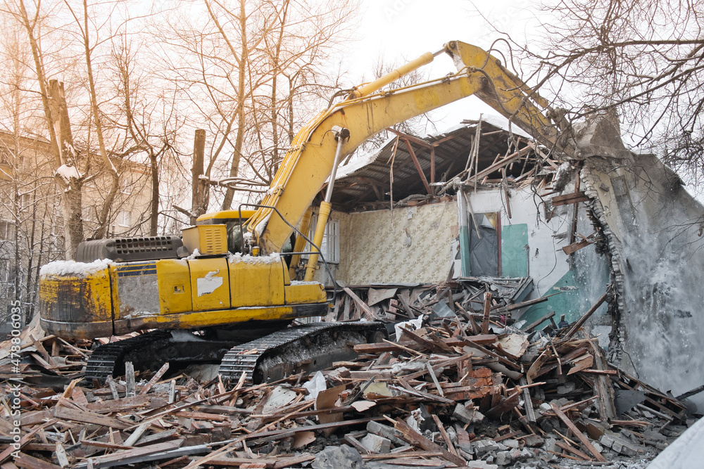 Building demolition. Excavator breaks old two-storey house. Industrial cityscape with destroy process.