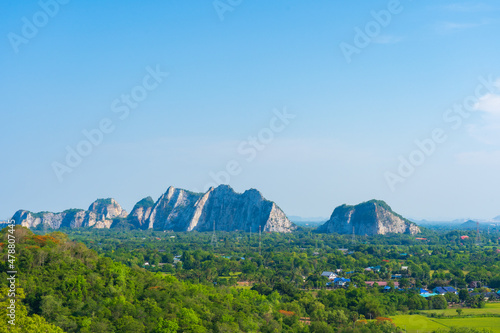 A large rocky mountain stands in the midst of forests and urban villages in Thailand in the afternoon of summer.