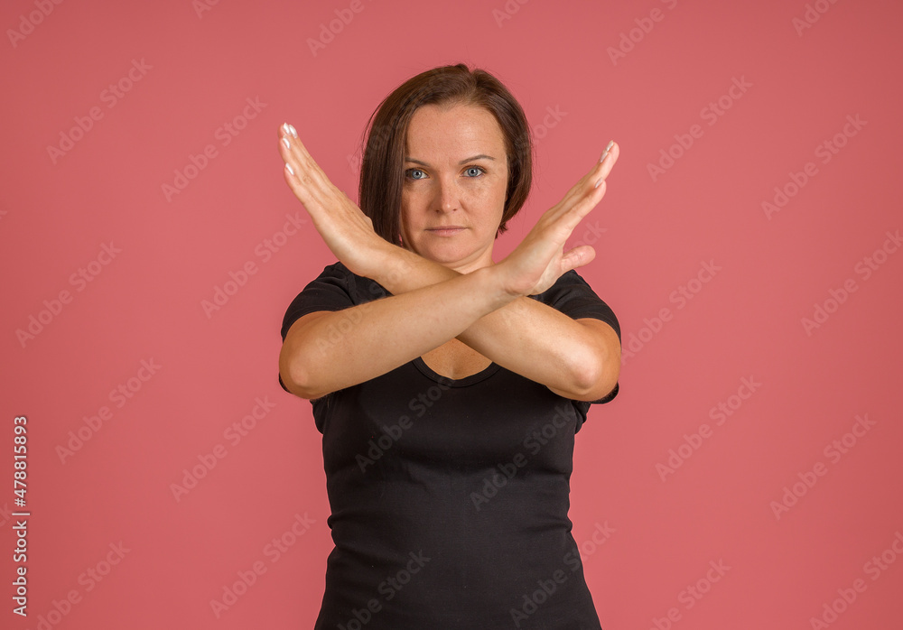 woman in black T-shirt with her arms crossed in front of her, X sign, pink background woman in black T-shirt with her arms crossed in front of her, X sign, pink background