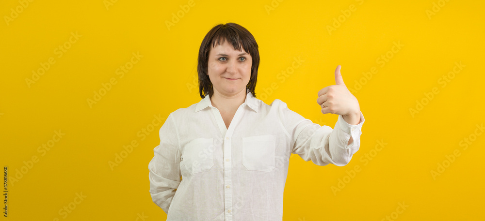 woman in white shirt shows thumb up on yellow background woman in white shirt shows thumb up on yellow background