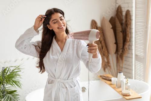 Obraz na plátně Pretty Brunette Female Drying And Styling Hair With Hairdryer Indoor