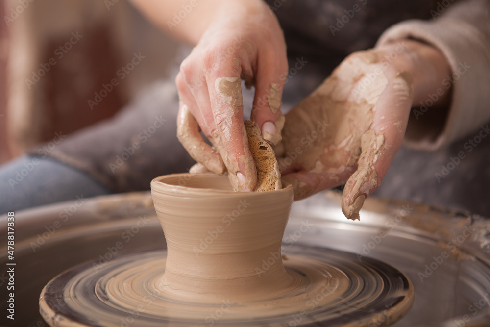 Unrecognizable woman making pottery, using potters wheel to shap clay mug