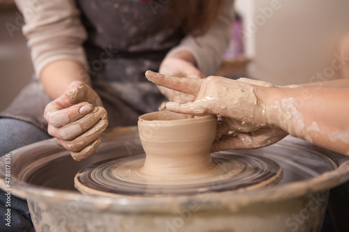 Cropped close up of unrecognizable potter showing her student how to throw pot on potters wheel