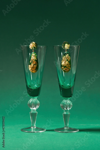 Studio shot of stylish handmade dangle earrings made of epoxy resin with golden foil inside on wine glasses isolated over green background photo