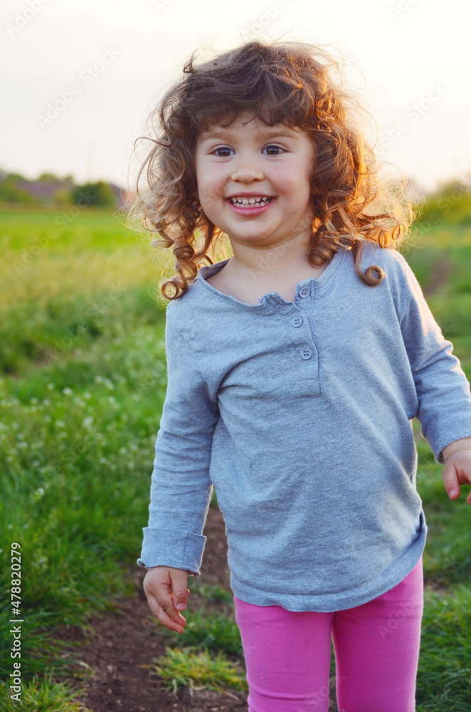 Portrait of Happy Toddler Girl Smiling Outdoor .Blond Kid with Curly Hair on a summer meadow Portrait of Happy Toddler Girl Smiling Outdoor .Blond Kid with Curly Hair on a summer meadow