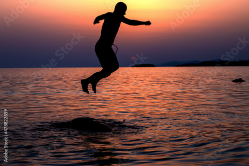 A boy is jumping of the rock in the sea