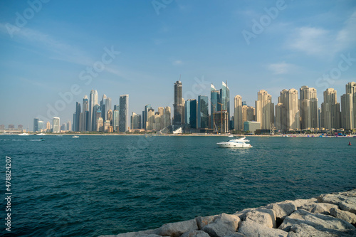 Iconic view to the Dubai Marina skyline, from Greenwaters island. Shot at bright summer day, with white speed boat passing Gulf sea.