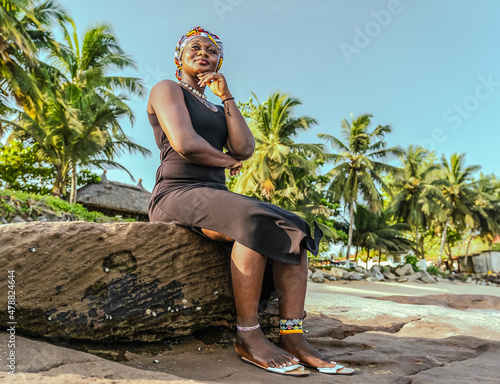 African woman with headdress sitting on a rock by the tropical beach in Takoradi Ghana West Africa photo