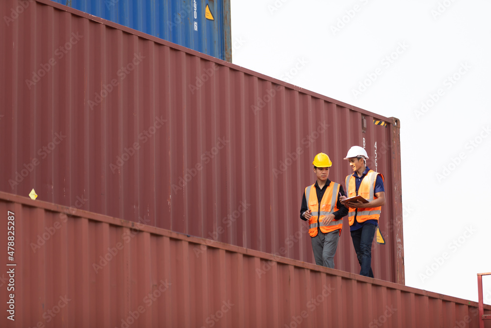 Two Asian man engineer worker wearing hardhat safety helmet and vest working in logistic shipping yard. Marine and carrier insurance concept. Cargo container yard. Two Asian man engineer worker wearing hardhat safety helmet and vest working in logistic shipping yard. Marine and carrier insurance concept. Cargo container yard.