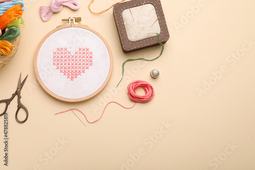 Flat lay composition with embroidery and different sewing accessories on beige background. Space for text