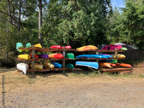Kayaks in a rack, with green foliage behind, bright colors