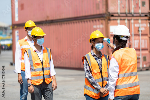 female manager measures temperature with a thermometer for employees before entering a container yard. import and export concept. Professional engineering team.