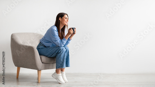 Quadro su tela Full length of young woman having coffee break in cozy armchair against white st