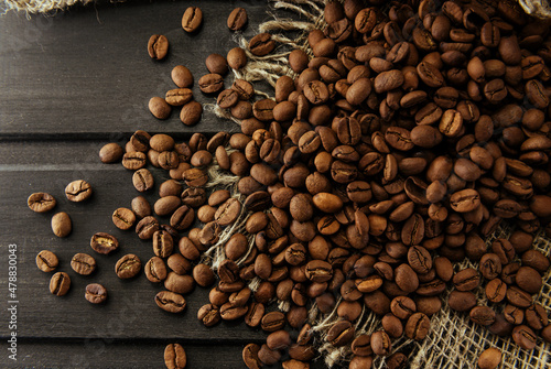 Coffee beans . Coffee beans are scattered and lie on a burlap on a wooden dark background close-up