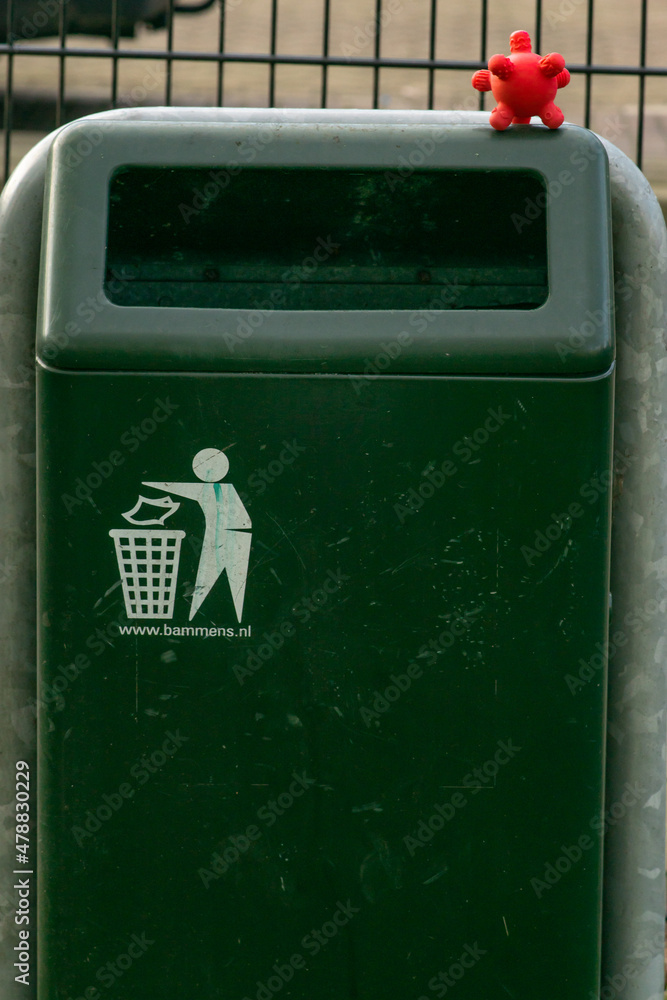 Coronavirus covid-19 cell toy on a rubbish bin on the street. Infection danger caused by infrastructure of public space in the city.