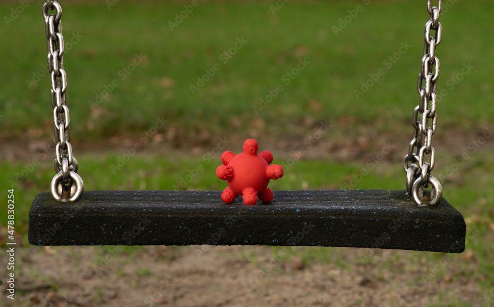 Coronavirus spread among children - rubber toy looking like covid19 cell on a swing at the playground at school.