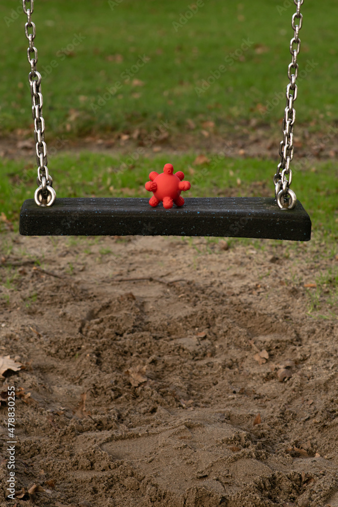 Coronavirus spread among children - rubber toy looking like covid-19 cell on a swing at the playground at school. Vertical photo.
