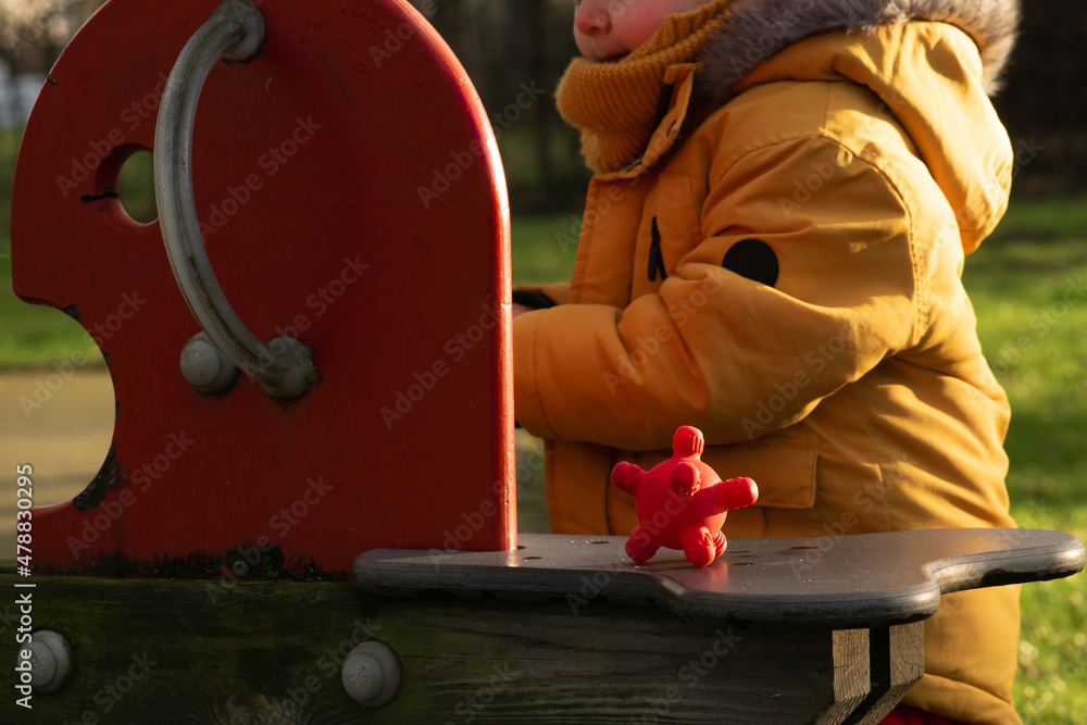 Virus and bacterial diseases spreading among children at school. Red rubber corona ball on a wooden swing at the kindergarten, next to little kid playing.