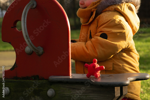 Obraz na płótnie Virus and bacterial diseases spreading among children at school. Red rubber corona ball on a wooden swing at the kindergarten, next to little kid playing. w salonie