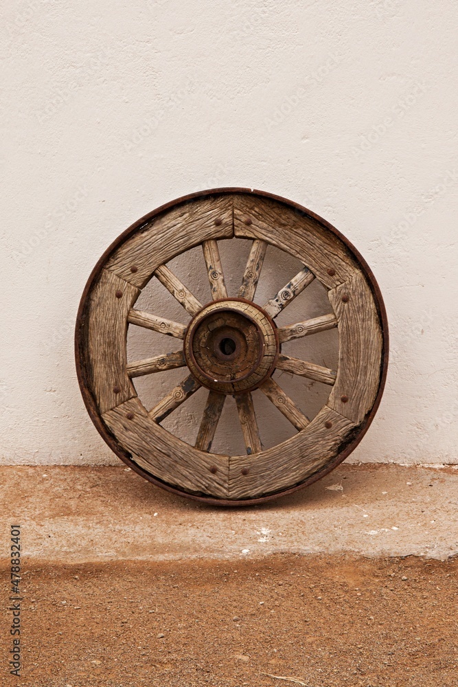 Isolated old wooden wagon wheel leaning against a white wall