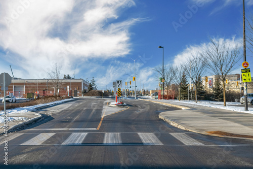 Empty roadway intersection  winter daytime  traffic signage  traffic lights and crosswalk markings  blue sky with clouds and buildings in background  nobody