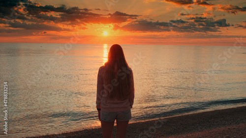 Medium shot of admiring sunrise on seashore woman raising up her hands. Back view