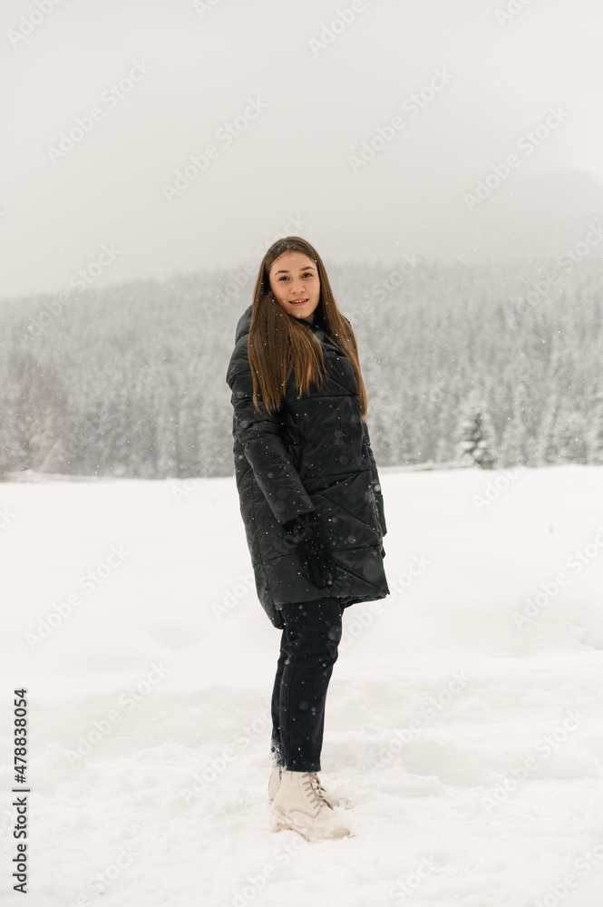 Beautiful girl walking in a snowfall. Young woman in black puffer jacket posing in the winter forest.Outdoor portrait of pretty brunette lady. Winter concept Beautiful girl walking in a snowfall. Young woman in black puffer jacket posing in the winter forest.Outdoor portrait of pretty brunette lady. Winter concept
