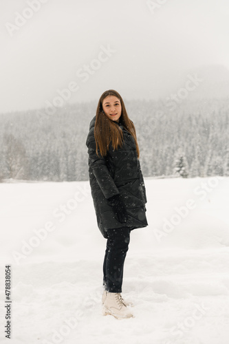 Beautiful girl walking in a snowfall. Young woman in black puffer jacket posing in the winter forest.Outdoor portrait of pretty brunette lady. Winter concept
