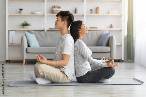 Asian man and woman sitting back to back, meditating